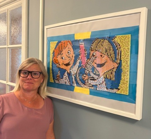 Jessica Melin står intill tavla med Ville och Vilma. Foto.